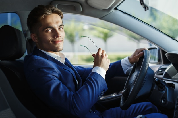 Apuesto joven empresario se sienta en el volante dentro del coche