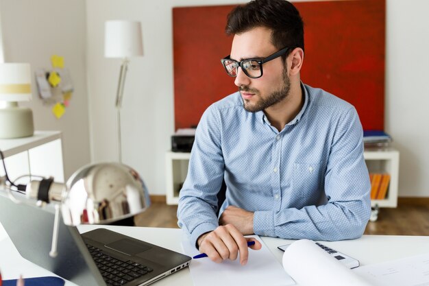 Apuesto joven empresario trabajando con ordenador portátil en la oficina.