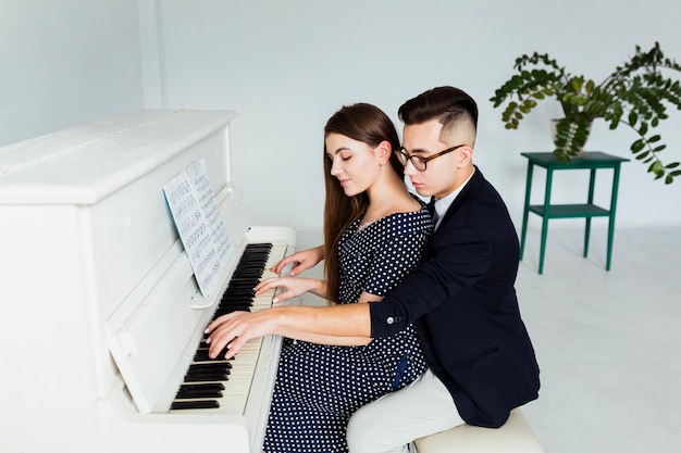 Apuesto joven enseñando a su novia a tocar el piano