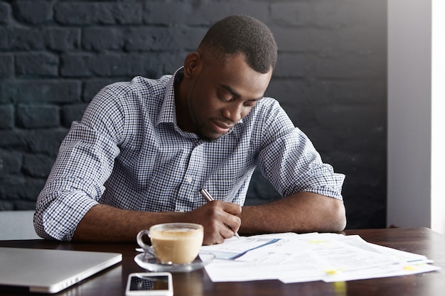 Apuesto joven estudiante afroamericano en camisa subyacente información importante en papel