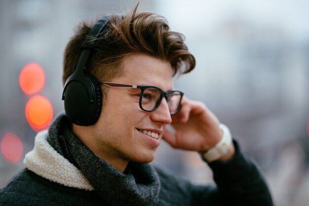 Apuesto joven feliz en anteojos, escuchando música en auriculares