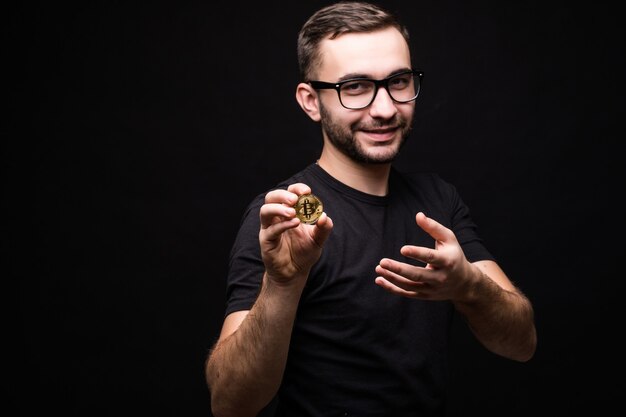 Apuesto joven con gafas usa camisa negra presente bitcoin aislado en negro