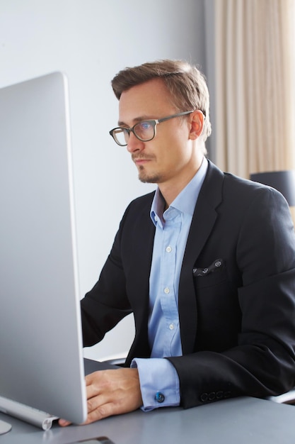 Un apuesto joven hombre de negocios con traje que trabaja con una computadora en la oficina.