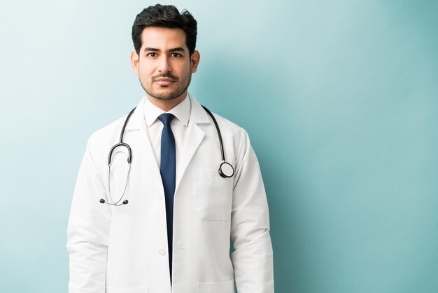 Apuesto joven médico masculino con estetoscopio de pie contra el fondo azul.