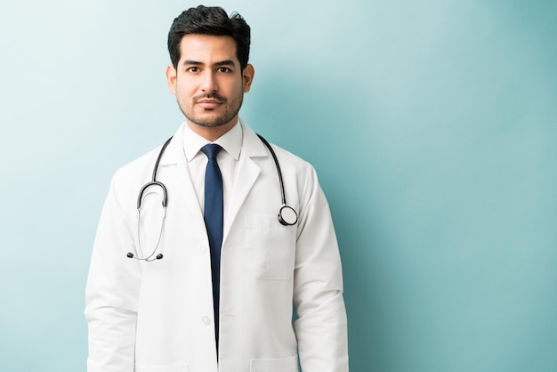 Apuesto joven médico masculino con estetoscopio de pie contra el fondo azul.