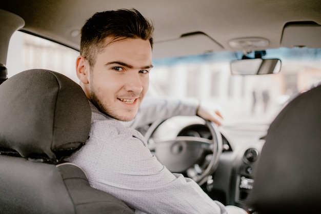 Apuesto joven mirando a la cámara, sentado en un automóvil, vista desde el asiento trasero