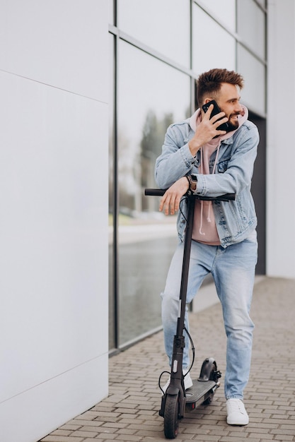 Foto gratuita apuesto joven montando scooter eléctrico y usando el teléfono