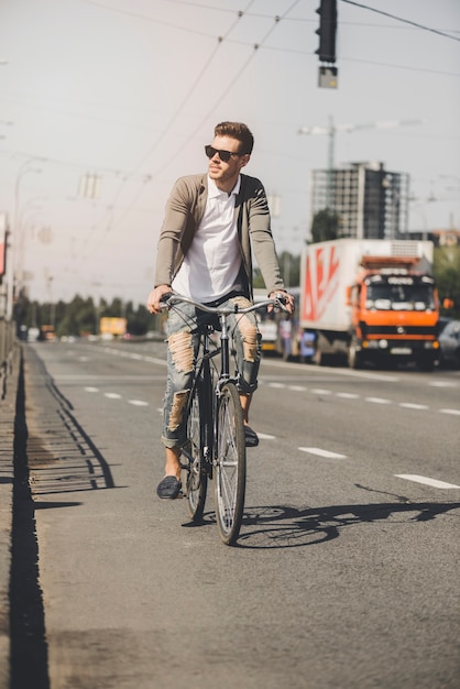 Foto gratuita apuesto joven montar bicicleta en la carretera de la ciudad