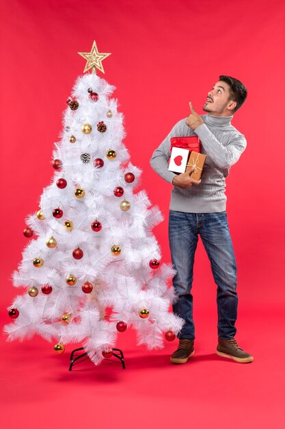 Apuesto joven de pie cerca del árbol de año nuevo blanco decorado