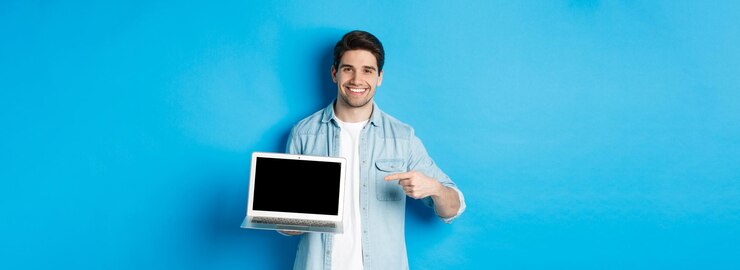 Foto gratuito apuesto joven señalando con el dedo a la pantalla de la computadora sonriendo complacido mostrando promoción en internet o