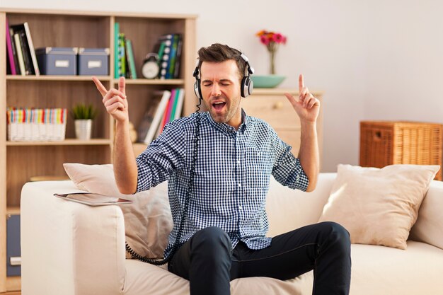 Apuesto joven sentado en su sofá y escuchando música