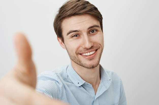 Apuesto joven con sonrisa feliz, extender la mano hacia adelante