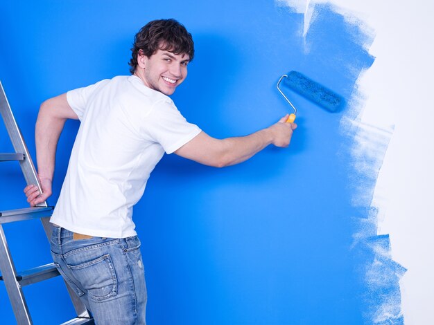 Apuesto joven con sonrisa feliz pintando la pared