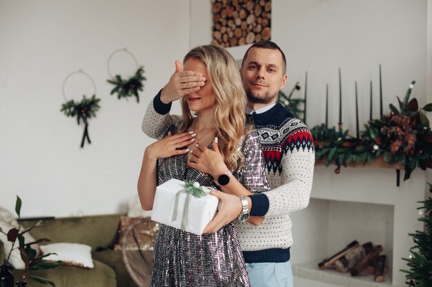 Apuesto joven sosteniendo la mano sobre los ojos de su novia mientras le da un regalo especial de Navidad