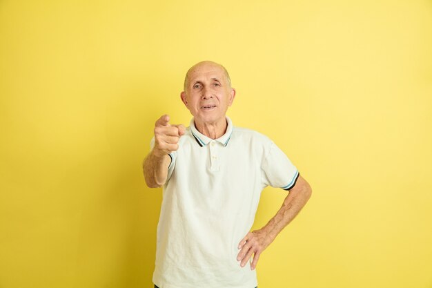 Apuntando. Retrato de hombre mayor caucásico aislado sobre fondo amarillo de estudio. Hermoso modelo emocional masculino. Concepto de emociones humanas, expresión facial, ventas, bienestar, publicidad. Copyspace.