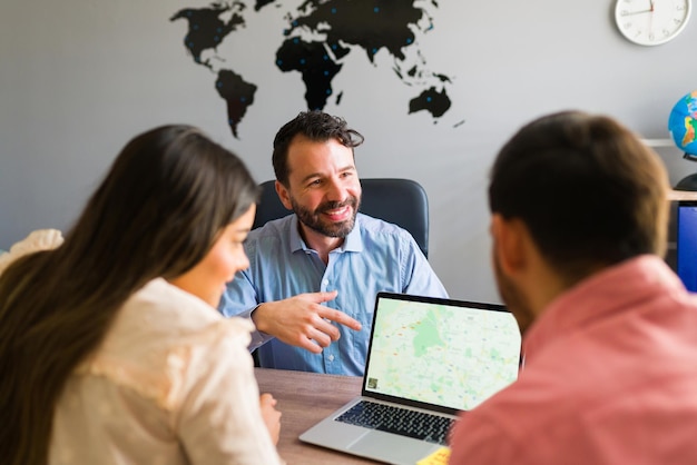 Aquí está su próximo destino de viaje. Vista trasera de una hermosa pareja mirando un mapa en una computadora portátil en la agencia de viajes y eligiendo dónde ir de vacaciones