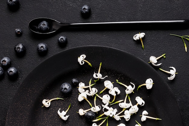 Arándanos planos en plato oscuro con flores.