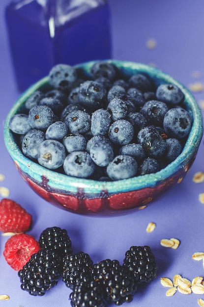 Arándanos en un plato y moras y frambuesas sobre un fondo azul. Cosecha de verano.