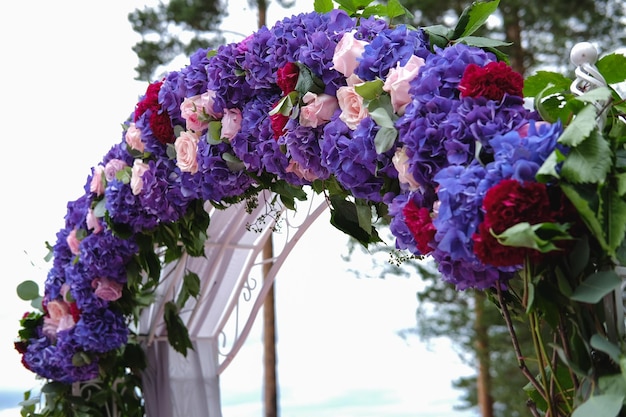 Arco de bodas y sillas grises con peonías de pie en el área de la ceremonia en el bosque