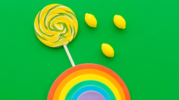 Foto gratuita arco iris cerca de caramelos de lollipop y limón sobre fondo verde