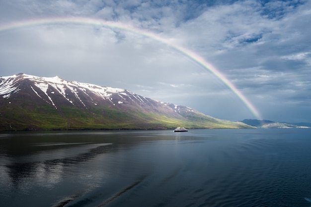 El arco iris sobre el mar cerca de las montañas nevadas y un barco aislado