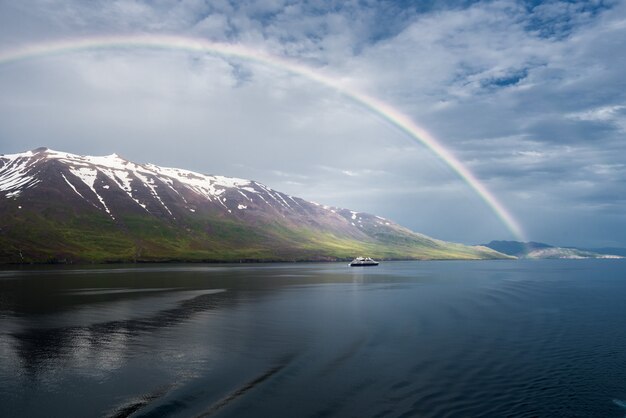 El arco iris sobre el mar cerca de las montañas nevadas y un barco aislado