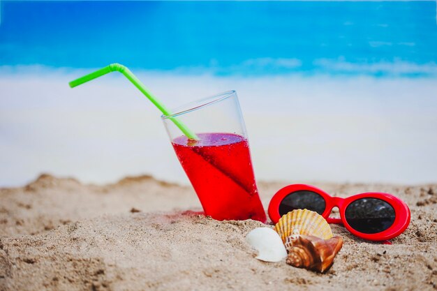 Arena con bebida, gafas de sol y conchas marinas
