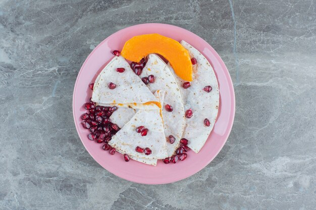 Arilos de granada y calabaza en rodajas con lavash en plato, sobre la mesa de mármol.