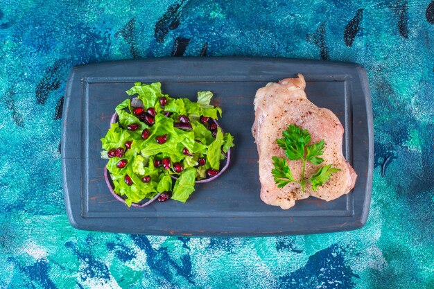 Arilos de granada, hojas de lechuga con aros de cebolla junto a la pechuga de pollo en una bandeja de madera