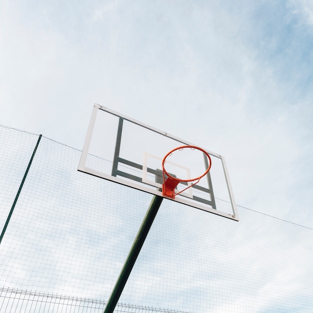 Aro de baloncesto y red en la cerca con vista al cielo