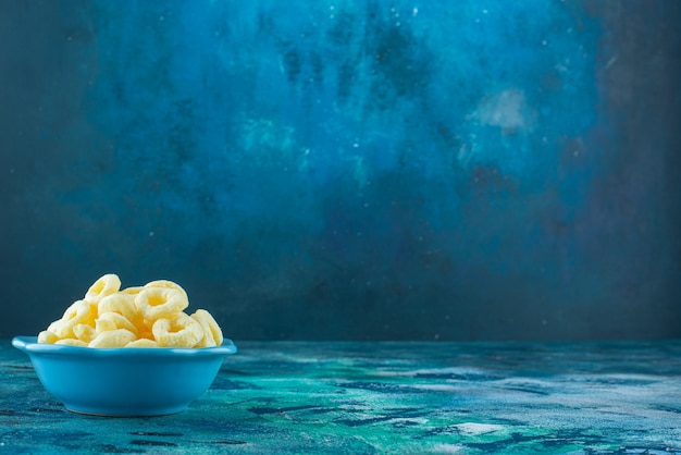Aros de maíz en un cuenco, sobre la mesa azul.