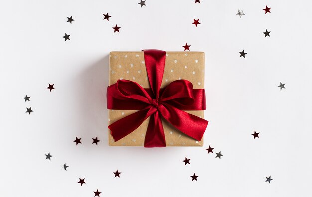 Arqueamiento rojo de la caja de regalo de vacaciones de Navidad en mesa festiva decorada con estrellas de destellos