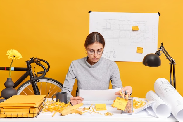 Arquitecta profesional seria concentrada en poses de papel en el dekstop con bocetos y planos desarrolla un nuevo proyecto