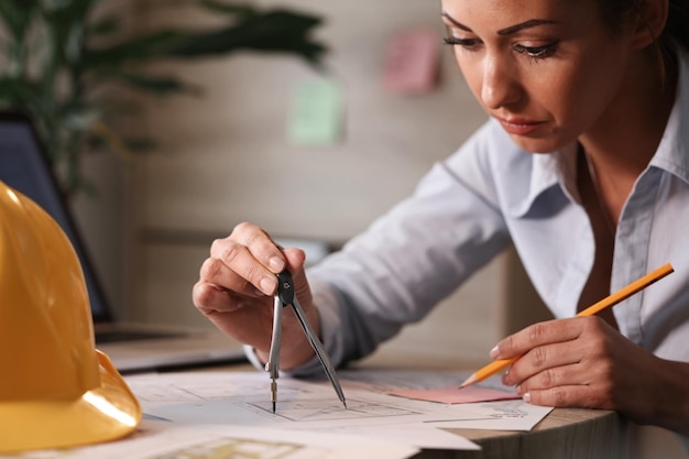 Arquitecto femenino trabajando en nuevas ideas y usando calibre mientras dibuja planes de proyecto en la oficina