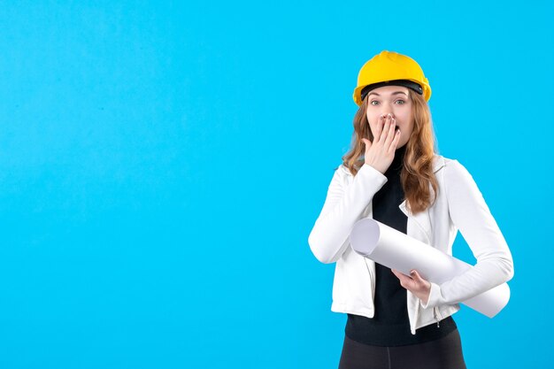 Arquitecto femenino de vista frontal en plan de explotación de casco amarillo sorprendido en azul