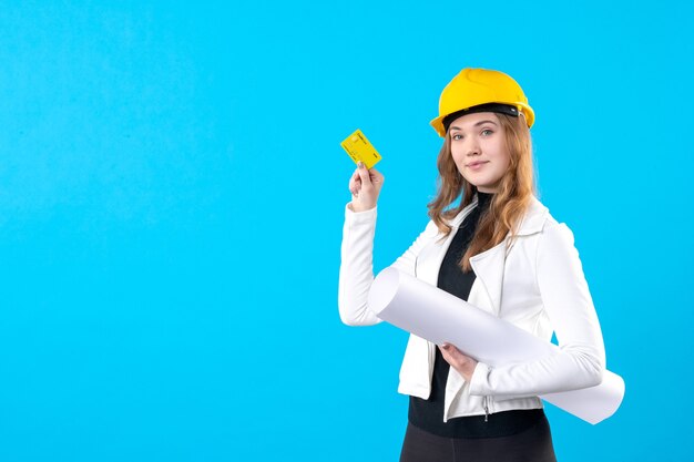 Arquitecto femenino de la vista frontal que sostiene el plan y la tarjeta bancaria en el azul