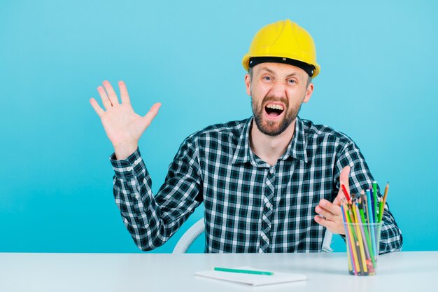 El arquitecto gritando está abriendo y levantando su puñado sobre fondo azul.