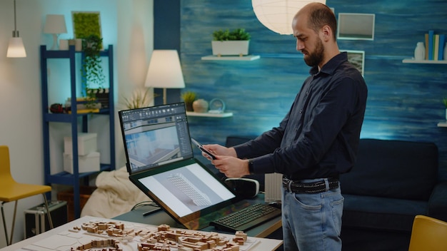 Arquitecto hombre mirando tableta con plan de diseño de edificio para proyecto de desarrollo en oficina de arquitectura. Joven ingeniero con dispositivo y modelo de plano para el diseño de la construcción