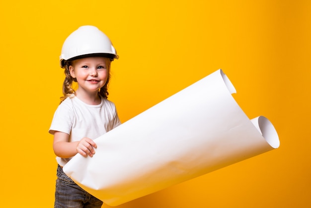 Arquitecto de niña en el casco de construcción con un cartel aislado en la pared amarilla
