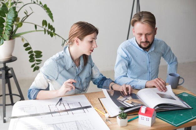 Arquitecto profesional masculino y femenino que mira el catálogo mientras trabaja en la oficina