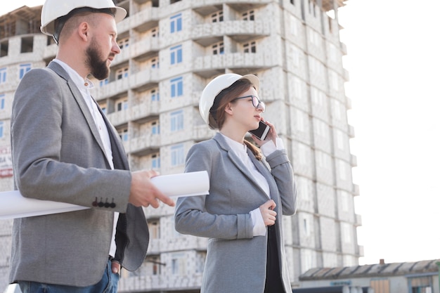 Foto gratuita arquitecto profesional de la mujer que habla en el teléfono móvil que se coloca con su colega masculino en el emplazamiento de la obra