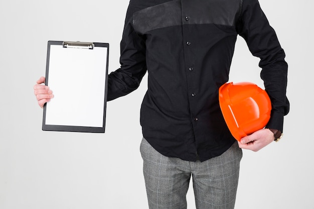 Un arquitecto que sostiene el tablero y el casco de protección sobre el fondo blanco