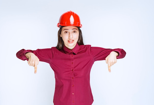 Arquitecto de sexo femenino confiado en rojo casco duro de pie y apuntando.