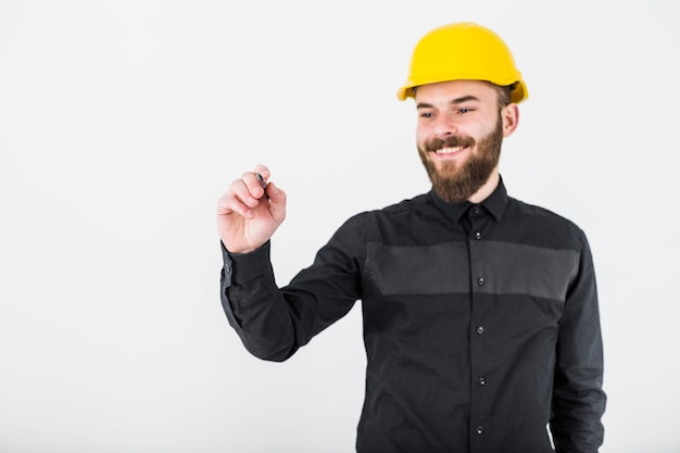 Un arquitecto de sexo masculino sonriente que lleva la pluma de tenencia amarilla del casco de protección para escribir