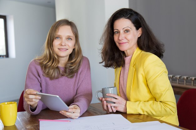 Arquitectos de sexo femenino sonrientes que beben té y que usan la tableta