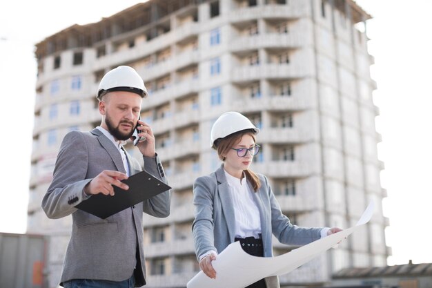 Arquitectura masculina que habla en el teléfono móvil que se coloca cerca de la arquitectura femenina que sostiene el modelo en el emplazamiento de la obra