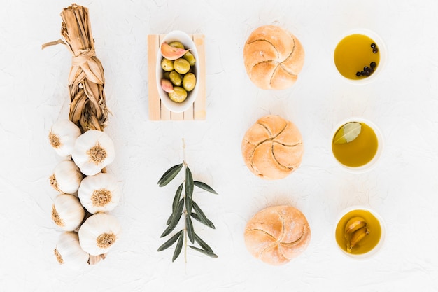 Foto gratuita arreglo de bollos y aceites con aceitunas y trenza de bulbos de ajo