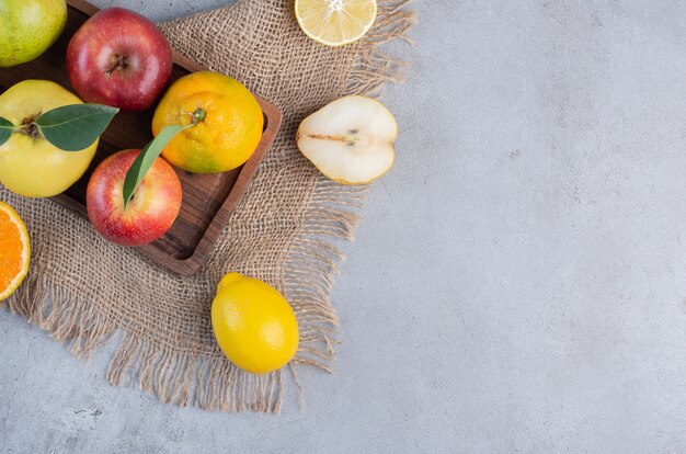 Un arreglo de diversas frutas sobre una tabla de madera y un trozo de tela sobre fondo de mármol.