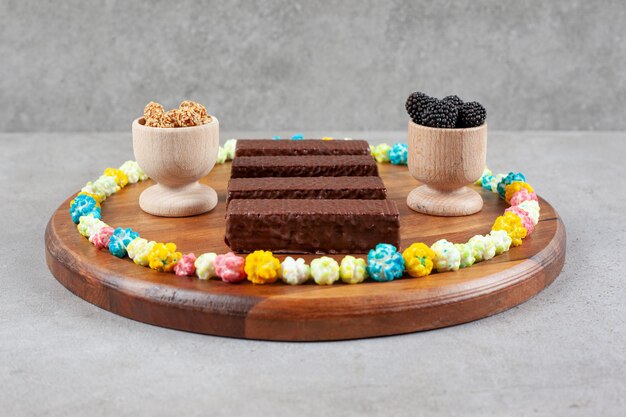 Un arreglo de gofres de chocolate y tazones de mullberries y cacahuetes glaseados anillados con dulces en una bandeja sobre la superficie de mármol