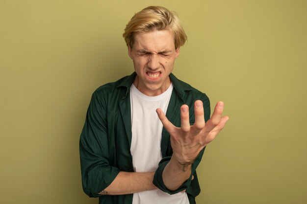 Arrepentido con los ojos cerrados joven chico rubio con camiseta verde tendiendo la mano